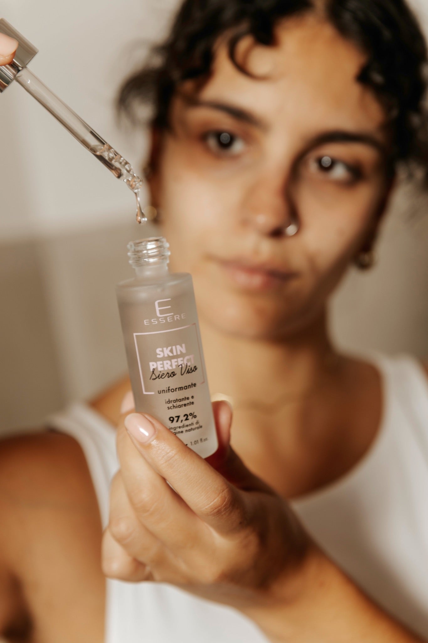 Donna mostra il siero viso Skin Perfect Essere Bio con il contagocce, sguardo verso l'obiettivo