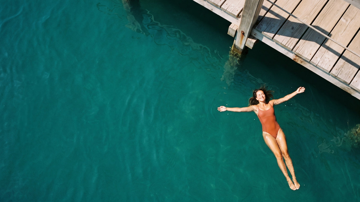 Donna che galleggia in mare turchese accanto a un pontile di legno