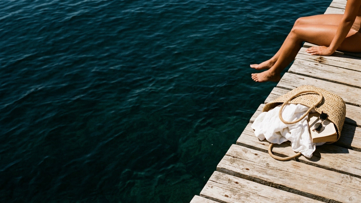 Pontile di legno sul mare, borsa di paglia con lino e libro