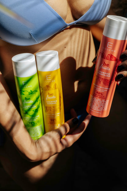 Shampoo Pompelmo Essere Bio Be Fruit in primo piano con gli altri due Be Fruit, tenuti in mano in flaconi colorati